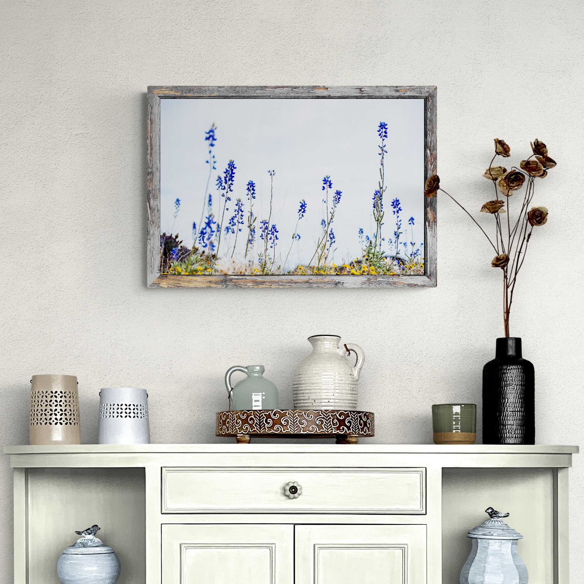 Framed artwork of bluebonnets on a wall above a white cabinet with decorative items.